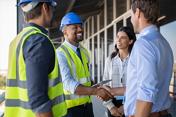Safety consulting company professional shaking hands with a client, while two others watch and smile.