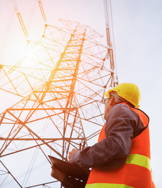 View from below of HazTek Inc. professional wearing hard hat and vest while applying expert safety solutions with large metal tower backdrop. 