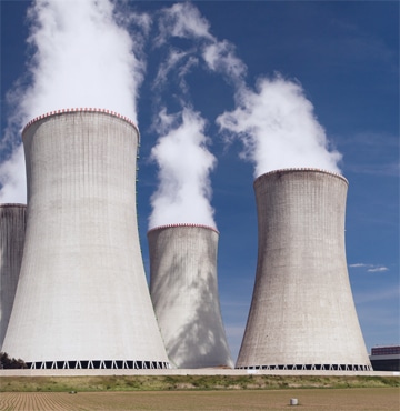 Four large silos releasing exhaust with blue sky backdrop.