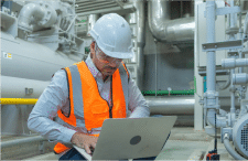 HazTek Inc. manager providing expert safety solutions on laptop at industrial site. 