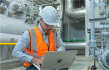 HazTek Inc. manager providing expert safety solutions on laptop at industrial site. 