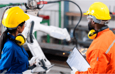 Two professionals wearing hard hats and leading safely by examining machine.