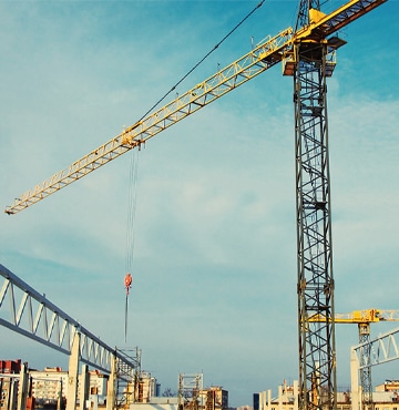 Large crane perched high above city landscape with cloudy sky backdrop. 