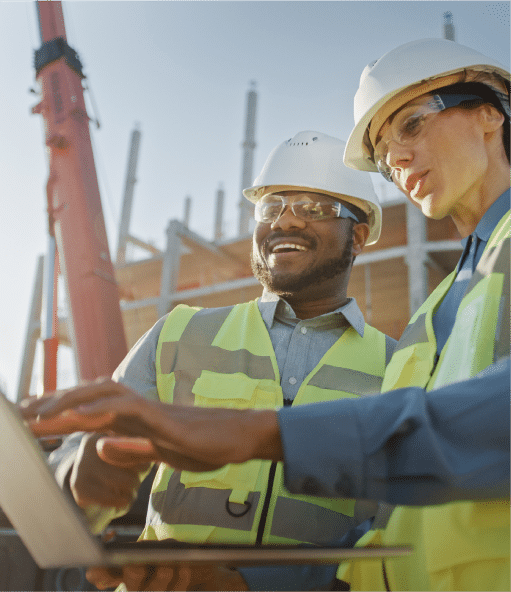 HazTek Inc. professionals leading safely by checking plans on laptop with construction site backdrop.