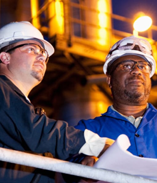 Two site safety managers wearing white hard hats while surveying project at night.